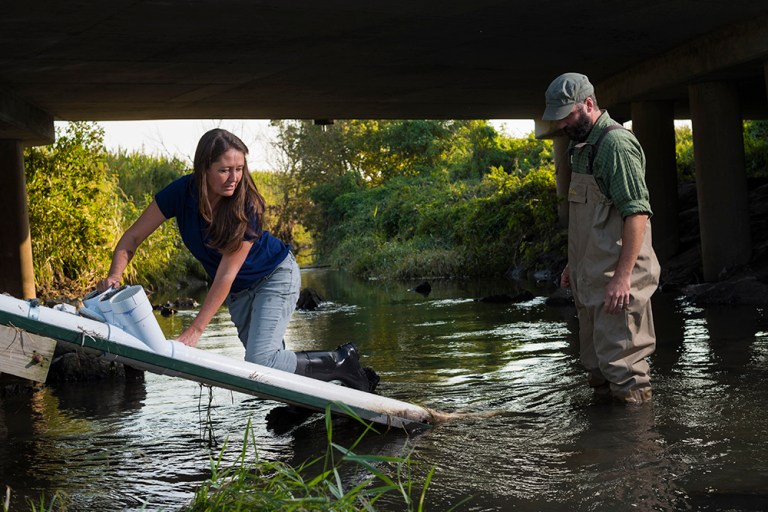 A woman standing in a river using the water quality sensor 