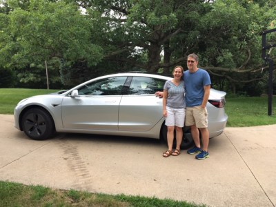 Two people stand in front of their tesla