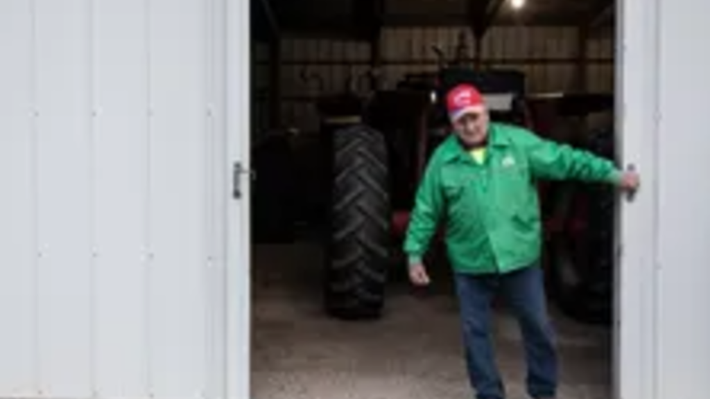 A farmer in a green coat pulls a big sliding door shut on the machine shed
